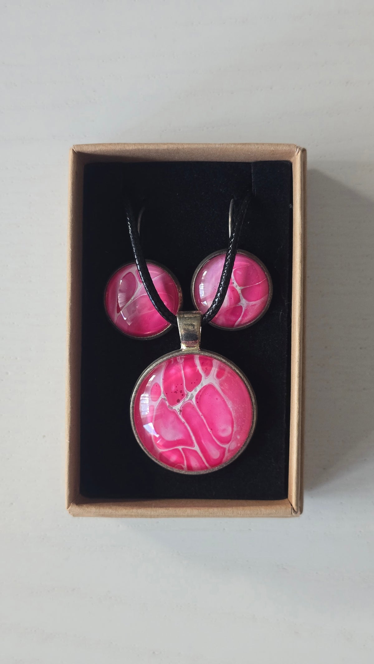 Rundes Cabochon-Schmuckset mit Anhänger und Ohrringen an schwarzem Band, mit organischem Muster in Fuchsia, Himbeerrosa und Pink sowie feinen hellen Linien.
