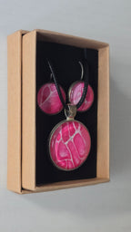 Rundes Cabochon-Schmuckset mit Anhänger und Ohrringen an schwarzem Band, mit organischem Muster in Fuchsia, Himbeerrosa und Pink sowie feinen hellen Linien.