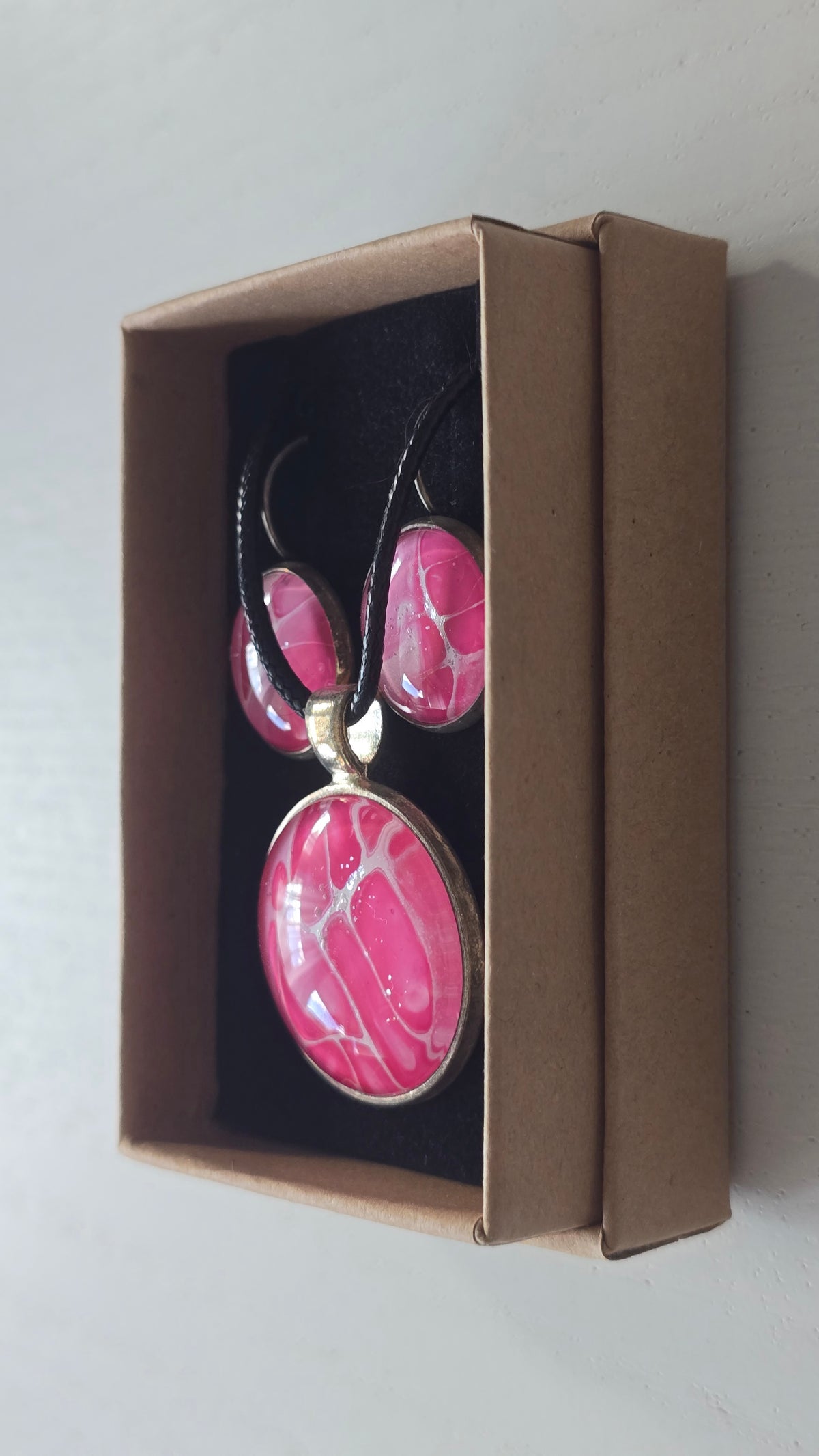 Rundes Cabochon-Schmuckset mit Anhänger und Ohrringen an schwarzem Band, mit organischem Muster in Fuchsia, Himbeerrosa und Pink sowie feinen hellen Linien.