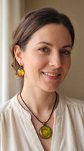 Frau trägt rundes Cabochon-Schmuckset mit Kette und passenden Ohrringen, leuchtend grün mit fliessenden roten, kupferfarbenen und orangefarbenen Strukturen.