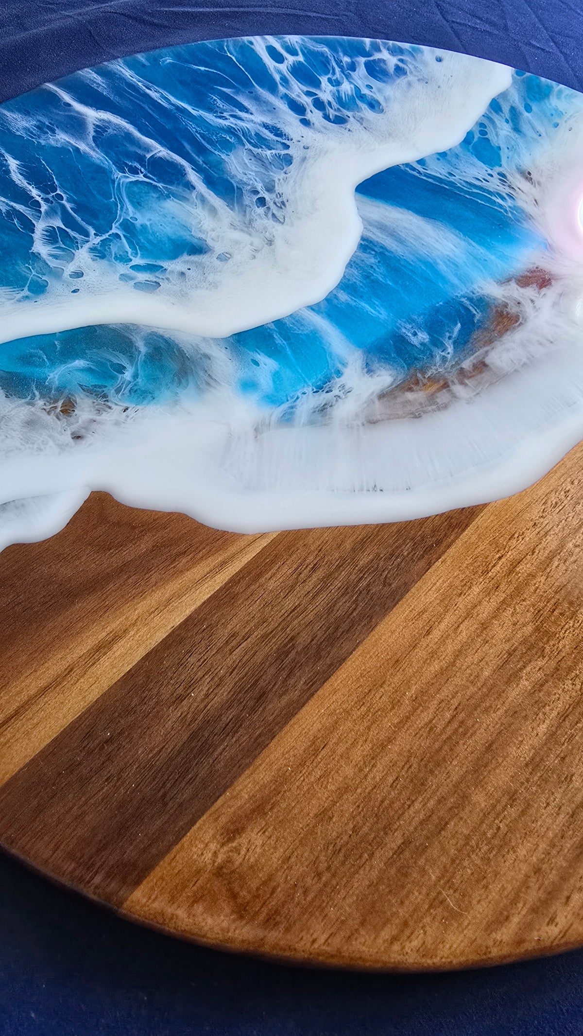 Rundes Resin Wandbild Solas Seafoam auf Holz mit blau-türkisem Meer, weissen Wellen, irisierenden Farbakzenten und sichtbarer Holzstruktur.