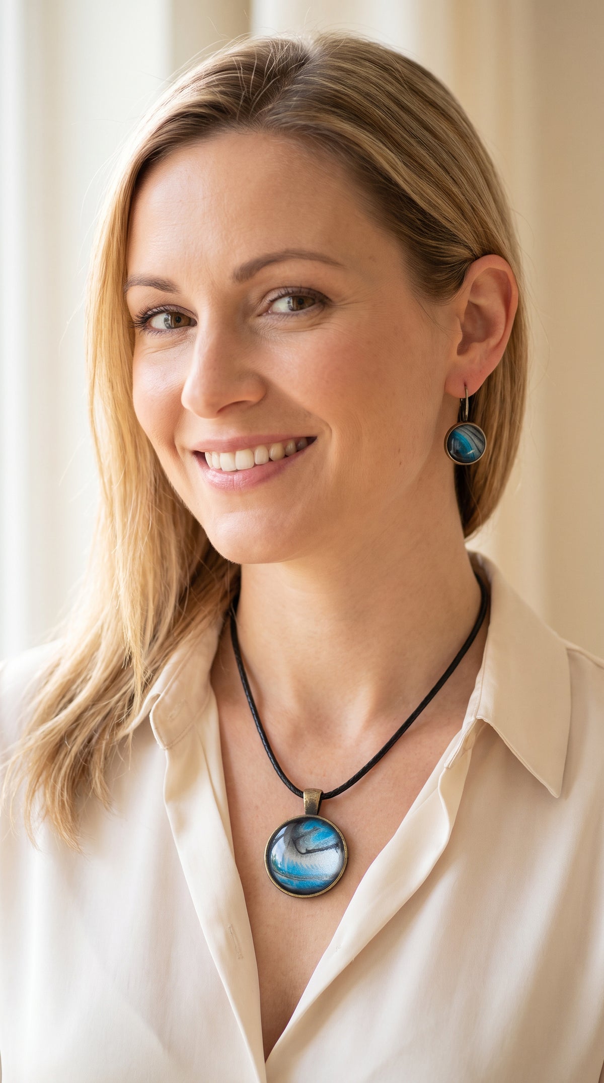 Frau trägt rundes Cabochon-Schmuckset mit Anhänger und Ohrringen an schwarzem Band, mit fliessendem Muster in Cyan und Blau, silbrigem Perlmuttschimmer und dunklen Linien.