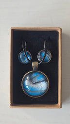 Rundes Cabochon-Schmuckset mit Anhänger und Ohrringen an schwarzem Band, mit fliessendem Muster in Cyan und Blau, silbrigem Perlmuttschimmer und dunklen Linien.