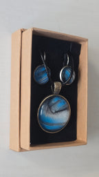 Rundes Cabochon-Schmuckset mit Anhänger und Ohrringen an schwarzem Band, mit fliessendem Muster in Cyan und Blau, silbrigem Perlmuttschimmer und dunklen Linien.