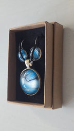 Rundes Cabochon-Schmuckset mit Anhänger und Ohrringen an schwarzem Band, mit fliessendem Muster in Cyan und Blau, silbrigem Perlmuttschimmer und dunklen Linien.