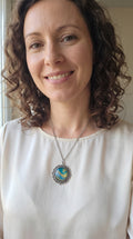 Frau trägt runde Cabochon Kette Solas Sunlit Current in Türkis, Blau und Gold mit verzierter silberfarbener Fassung und Metallkette.