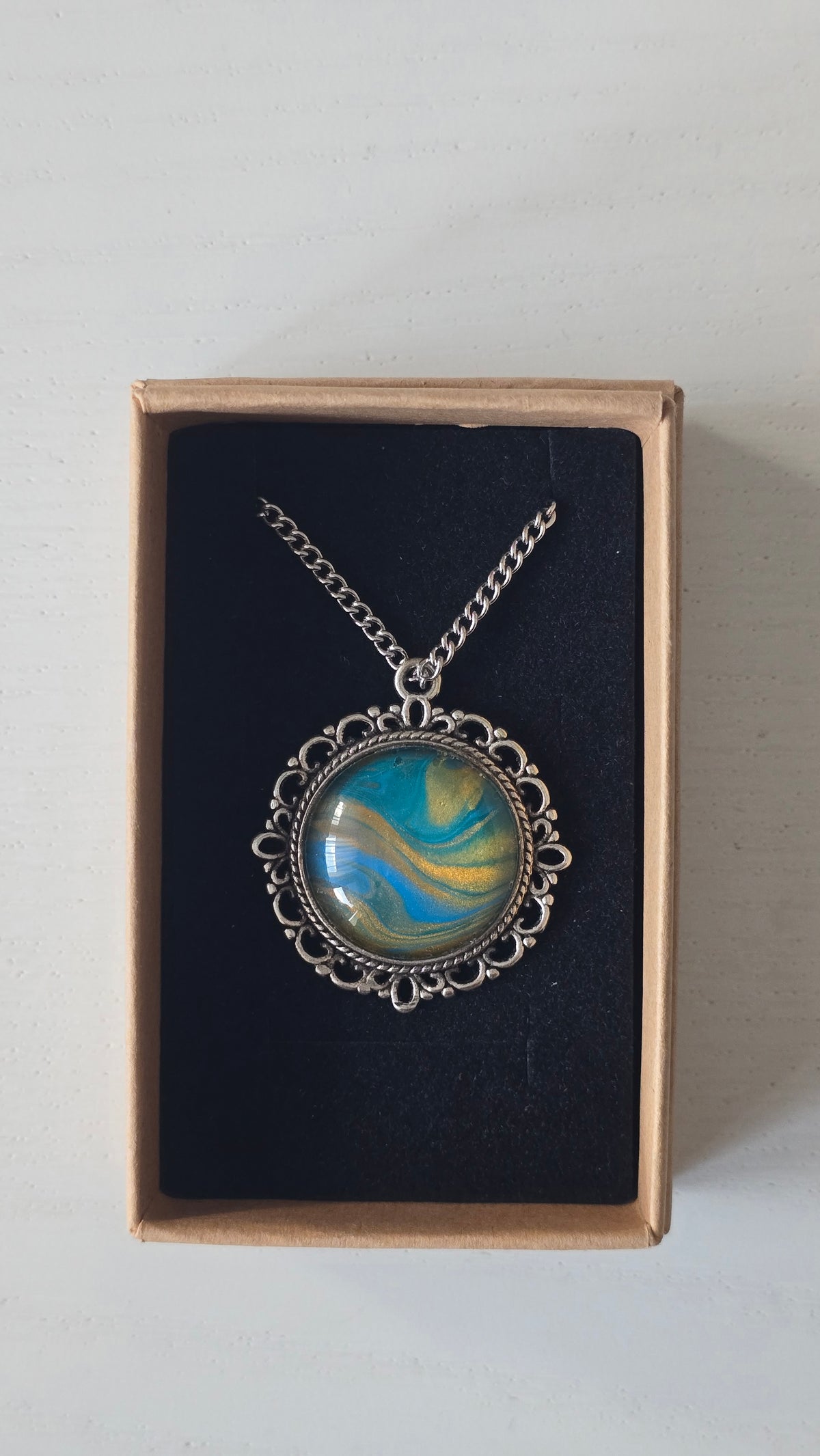 Runde Cabochon Kette Solas Sunlit Current in Türkis, Blau und Gold mit verzierter silberfarbener Fassung und Metallkette.