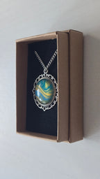 Runde Cabochon Kette Solas Sunlit Current in Türkis, Blau und Gold mit verzierter silberfarbener Fassung und Metallkette.