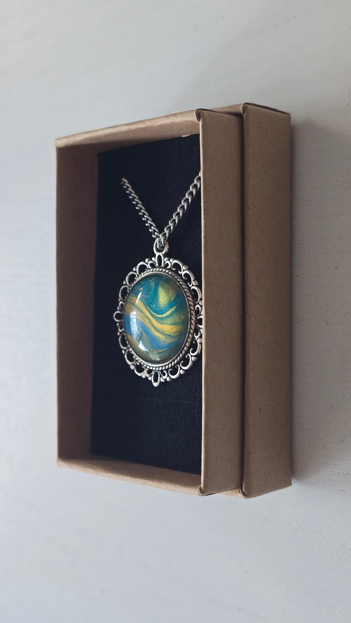 Runde Cabochon Kette Solas Sunlit Current in Türkis, Blau und Gold mit verzierter silberfarbener Fassung und Metallkette.
