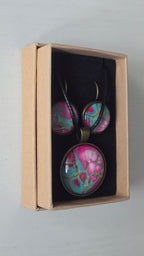 Cabochon-Schmuckset mit rundem Anhänger und zwei Ohrringen in Türkis und kräftigem Pink mit verzweigten goldenen Linien und schwarzem Textilband in einer Schachtel.