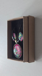 Cabochon-Schmuckset mit rundem Anhänger und zwei Ohrringen in Türkis und kräftigem Pink mit verzweigten goldenen Linien und schwarzem Textilband in einer Schachtel.