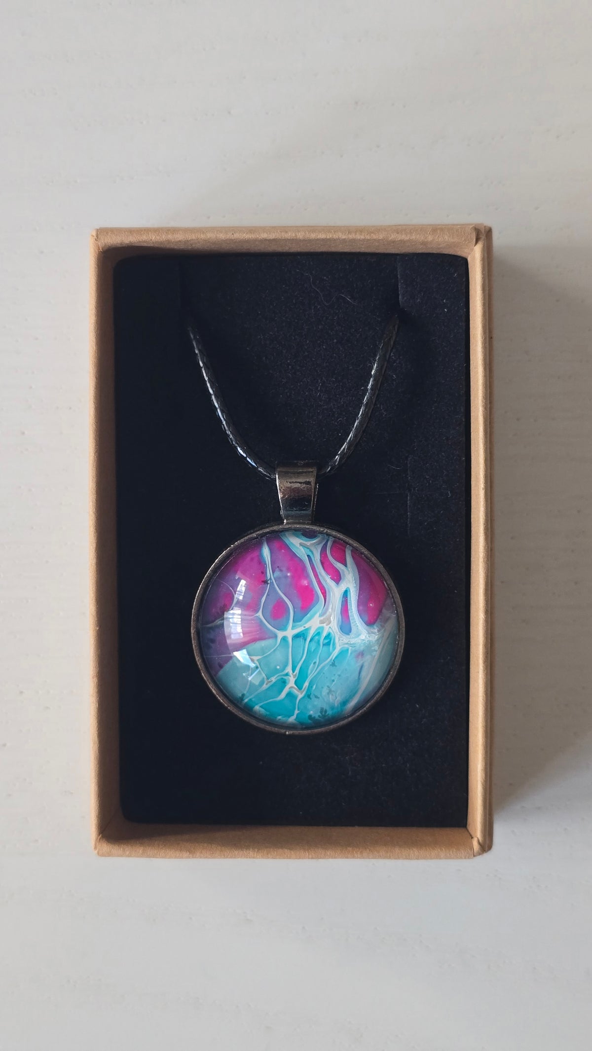 Runder Cabochon-Anhänger an schwarzem Band mit verzweigtem, organischem Muster in Türkis, Aqua, Fuchsia, Pink und hellen Linien.