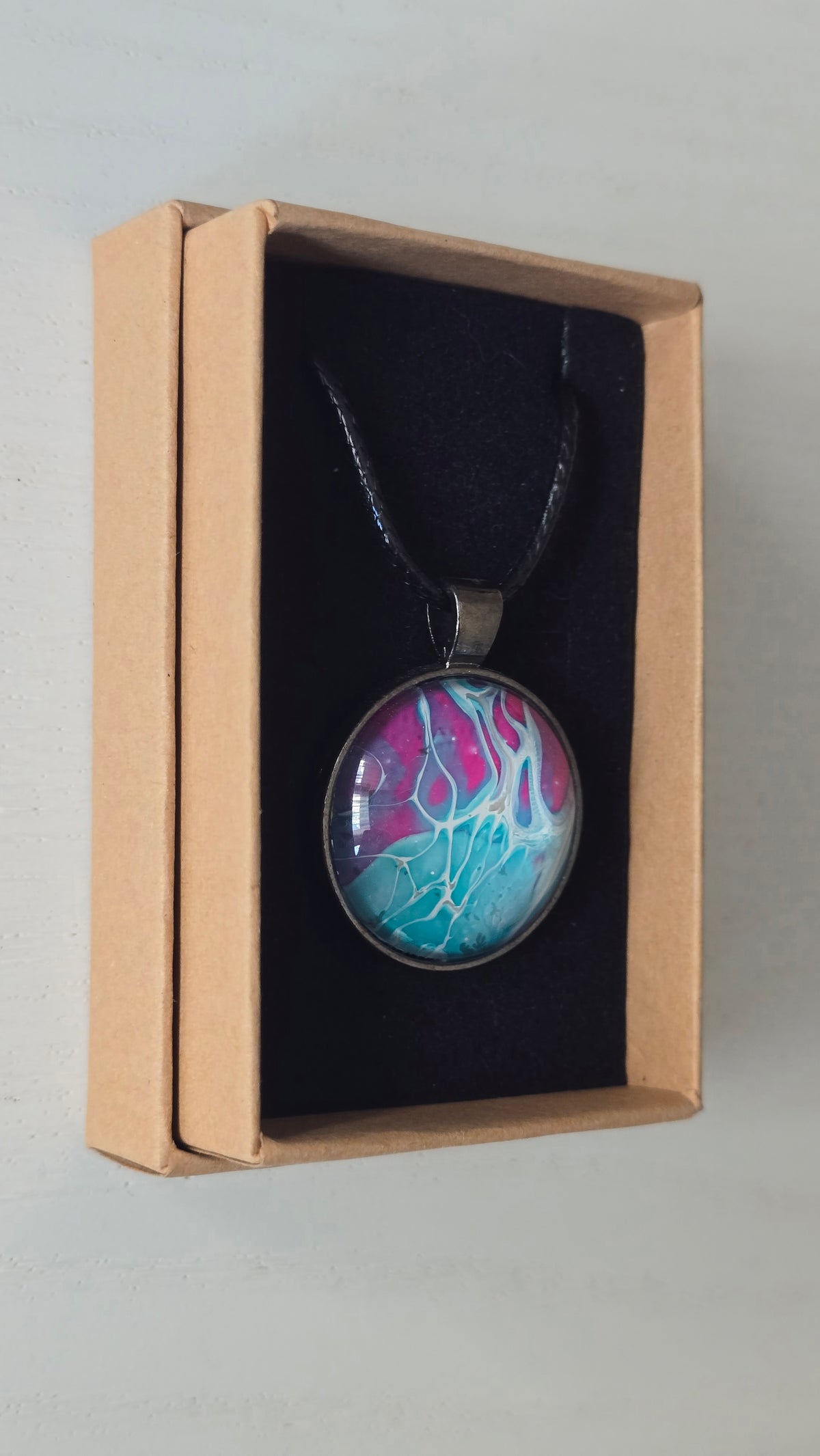 Runder Cabochon-Anhänger an schwarzem Band mit verzweigtem, organischem Muster in Türkis, Aqua, Fuchsia, Pink und hellen Linien.