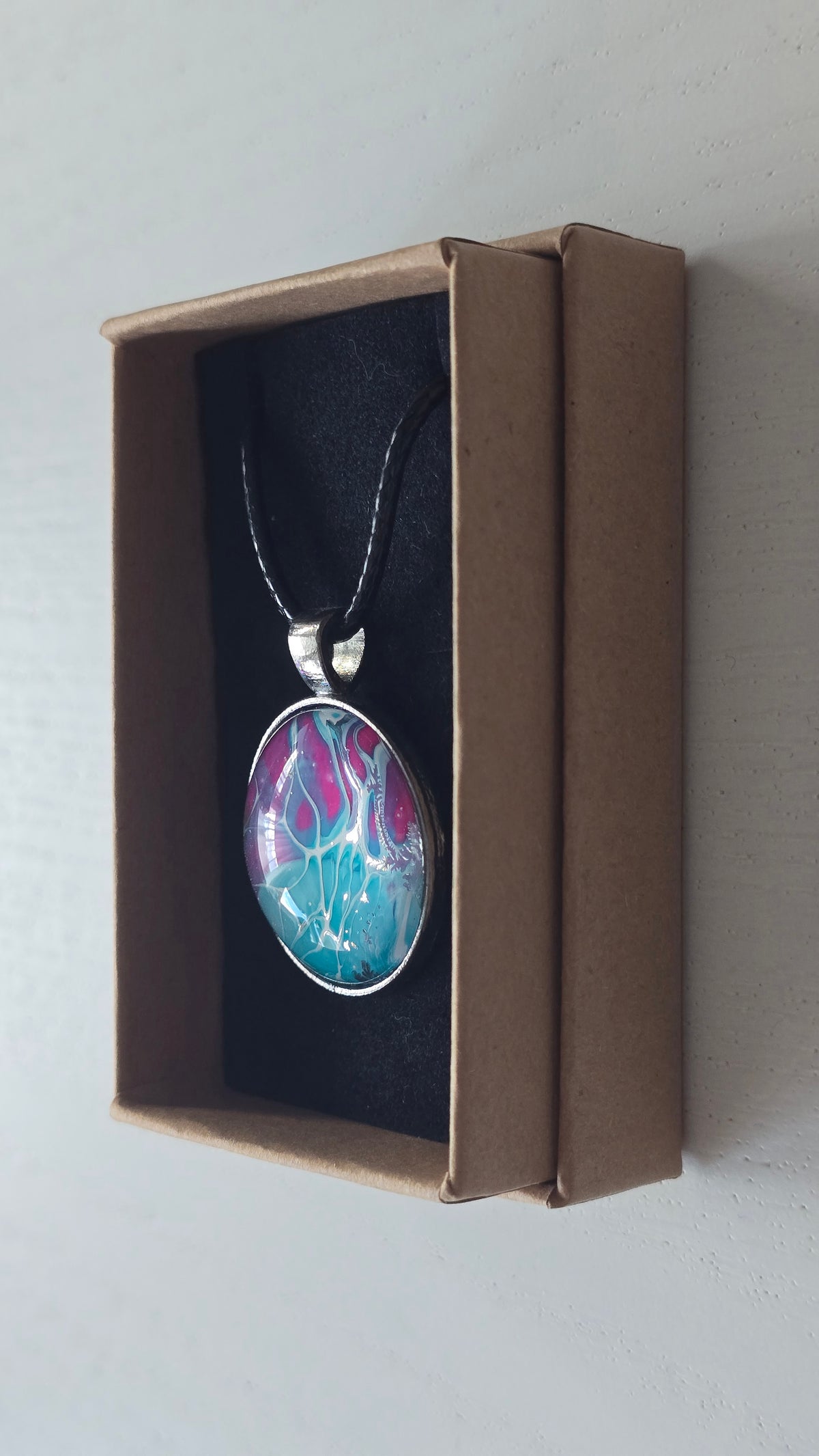 Runder Cabochon-Anhänger an schwarzem Band mit verzweigtem, organischem Muster in Türkis, Aqua, Fuchsia, Pink und hellen Linien.
