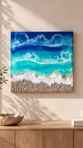 Handgefertigtes Resin-Meeresbild «Solas Turquoise Bay» mit türkisfarbenem Wasser, schäumenden Wellen und natürlichem Kieselstrand auf einem 40 × 40 cm grossen Gesso-Rahmen.