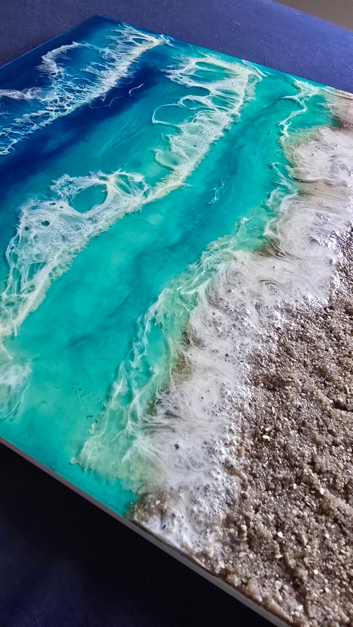 Handgefertigtes Resin-Meeresbild «Solas Turquoise Bay» mit türkisfarbenem Wasser, schäumenden Wellen und natürlichem Kieselstrand auf einem 40 × 40 cm grossen Gesso-Rahmen.