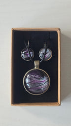 Rundes Cabochon-Schmuckset mit Anhänger und Ohrringen an schwarzem Band, mit fliessendem Muster in Violett, Pflaume, Silber und Schwarz.