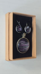 Rundes Cabochon-Schmuckset mit Anhänger und Ohrringen an schwarzem Band, mit fliessendem Muster in Violett, Pflaume, Silber und Schwarz.