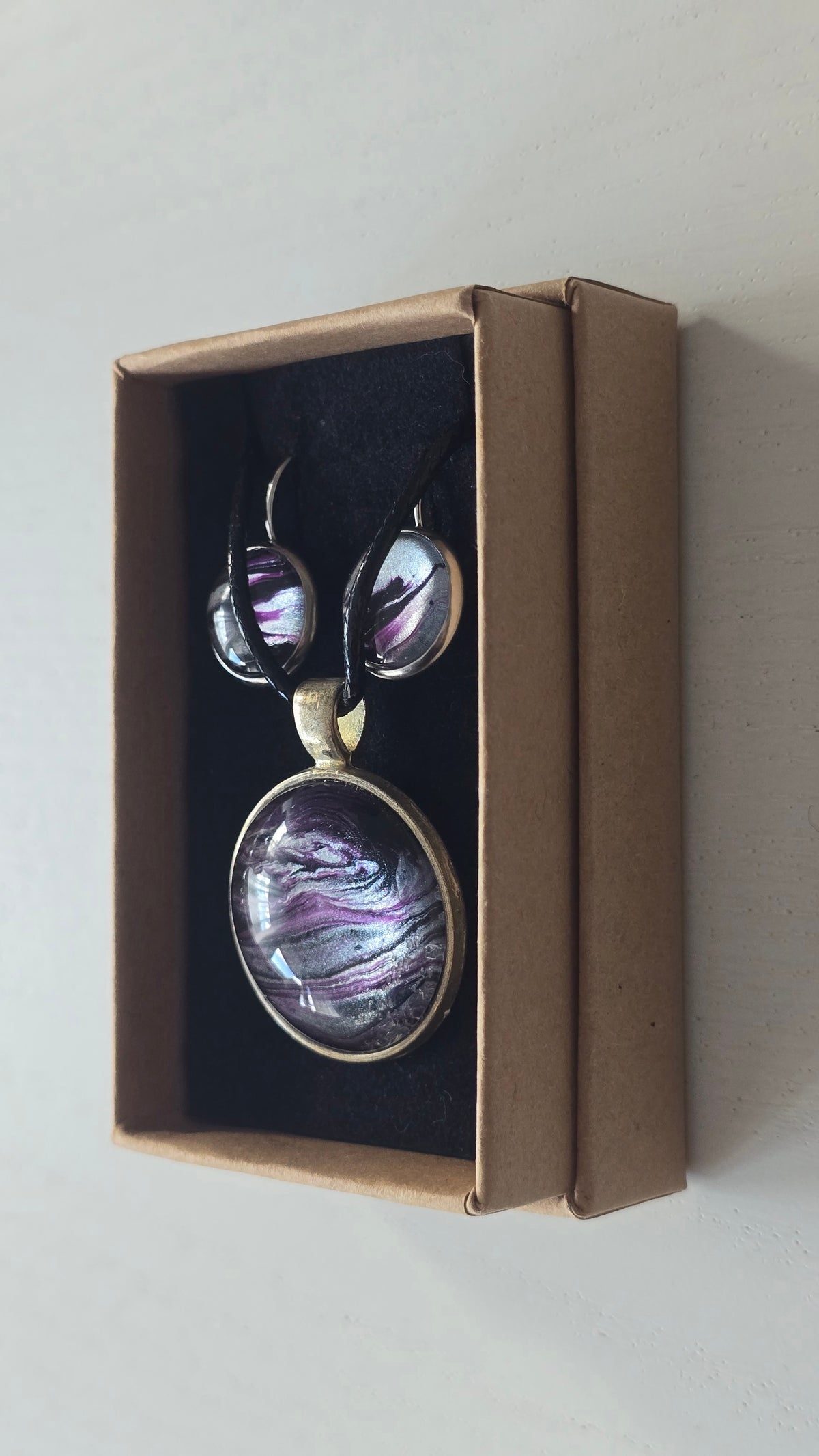 Rundes Cabochon-Schmuckset mit Anhänger und Ohrringen an schwarzem Band, mit fliessendem Muster in Violett, Pflaume, Silber und Schwarz.