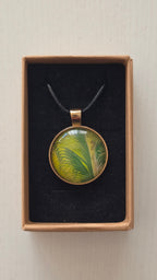 Runde Cabochon Kette Solas Wild Fern in verschiedenen Grün- und Goldtönen mit farnähnlicher Struktur, bronzefarbener Fassung und schwarzem Band.
