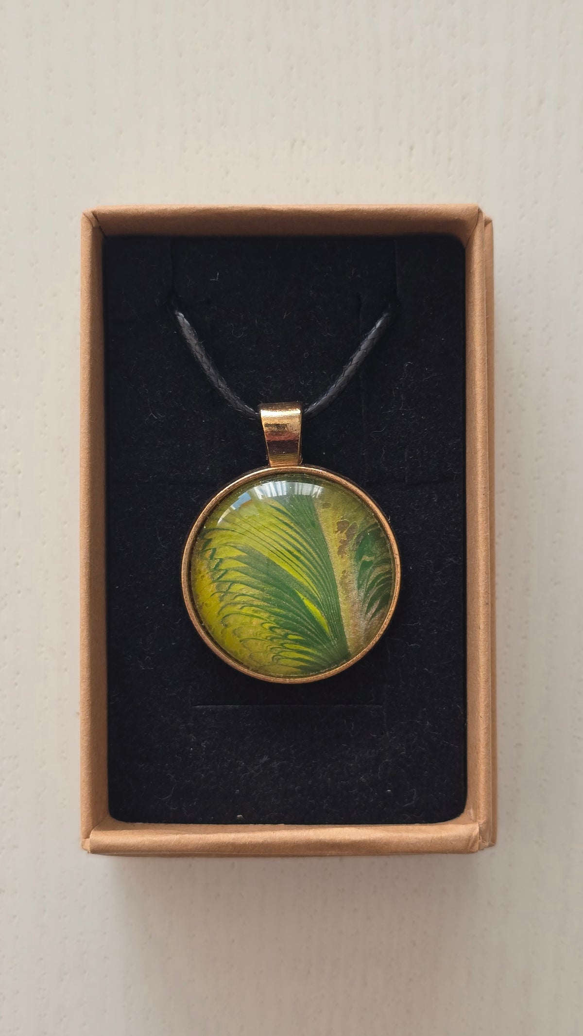 Runde Cabochon Kette Solas Wild Fern in verschiedenen Grün- und Goldtönen mit farnähnlicher Struktur, bronzefarbener Fassung und schwarzem Band.
