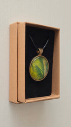 Runde Cabochon Kette Solas Wild Fern in verschiedenen Grün- und Goldtönen mit farnähnlicher Struktur, bronzefarbener Fassung und schwarzem Band.