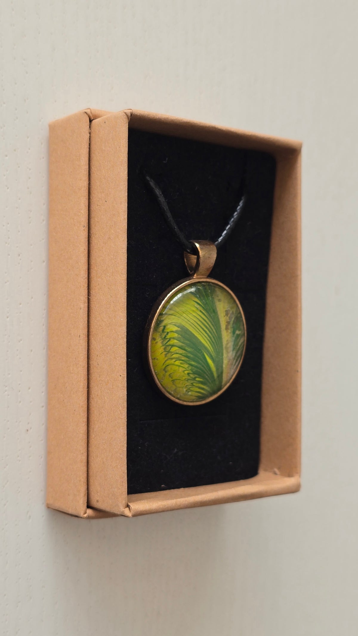 Runde Cabochon Kette Solas Wild Fern in verschiedenen Grün- und Goldtönen mit farnähnlicher Struktur, bronzefarbener Fassung und schwarzem Band.