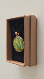 Runde Cabochon Kette Solas Wild Fern in verschiedenen Grün- und Goldtönen mit farnähnlicher Struktur, bronzefarbener Fassung und schwarzem Band.