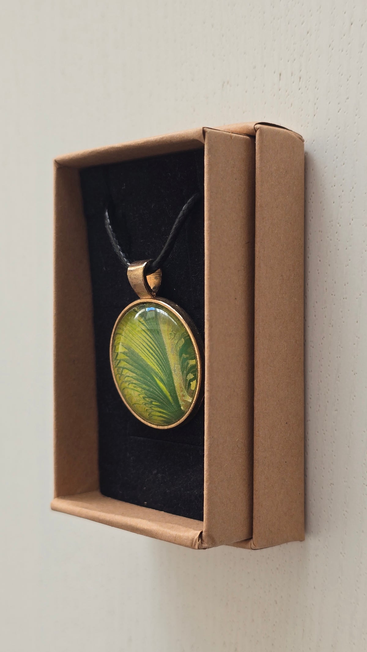 Runde Cabochon Kette Solas Wild Fern in verschiedenen Grün- und Goldtönen mit farnähnlicher Struktur, bronzefarbener Fassung und schwarzem Band.
