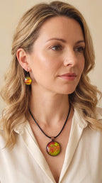 Frau trägt rundes Cabochon-Schmuckset mit Kette und zwei Ohrringen in leuchtendem Grün, Korallrot und Orange, mit feinen kupferfarbenen, organischen Linien.